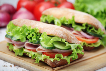 Two sandwiches with fresh vegetables, ham and cheese in ciabatta bread