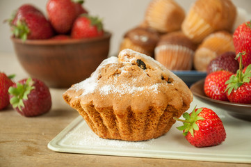 Fresh homemade delicious muffins with strawberries on kitchen table. Sweet dessert.