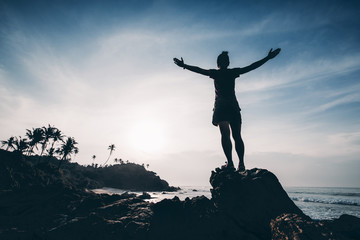 Strong woman outstretched arms on sunrise seaside rock cliff edge