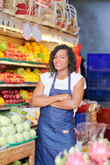 Pretty smiling young woman standing at shelves with fresh fruits