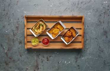 Fried chicken nuggets with legs and crispy octopus on wooden tray, top view, copy space. Street food concept, horizontal composition on stone background