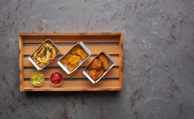 Fried chicken nuggets with legs and crispy octopus on wooden tray, top view, copy space. Street food concept, horizontal composition on stone background