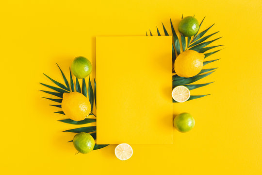Summer composition. Tropical palm leaves, citrus fruits, yellow paper blank on yellow background. Summer concept. Flat lay, top view, copy space