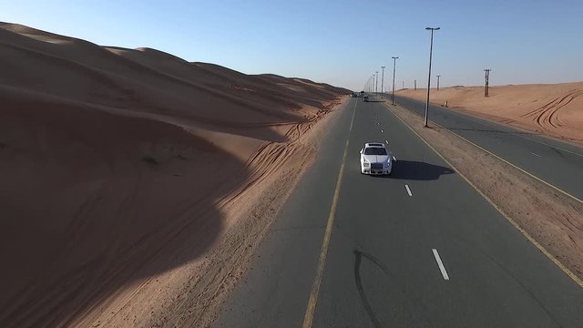 Aerial drone tracking shot of a fancy car driving along a desert highway in Dubai, United Arab Emirates