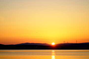 Fototapeta na wymiar silhouetted windmills on hill over orange colored sunrise sky