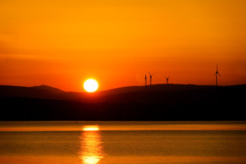 silhouetted windmills on hill over orange colored sunrise sky