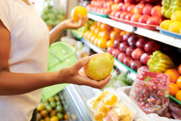 Hands of woman choosing what to buy in supermarket pear or orange