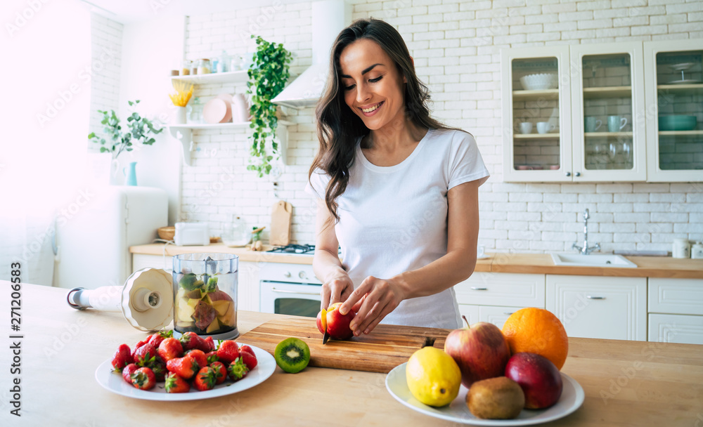 Wall mural beautiful woman making fruits smoothies with blender. healthy eating lifestyle concept portrait of b