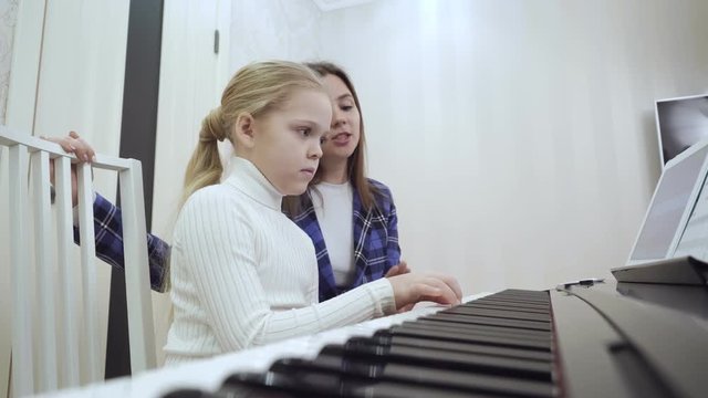 Young teacher with little cute girl playing on the electric piano.