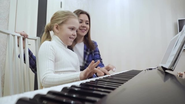 Young teacher with little cute girl playing on the electric piano.