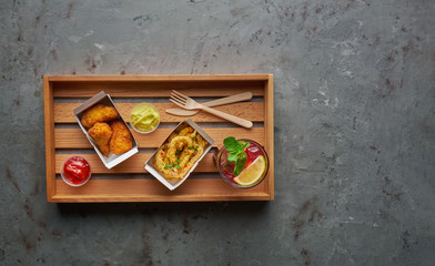 Fried chicken legs with crispy octopus and lemonade on wooden tray. Street food concept, horizontal composition on stone background