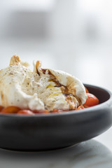 Burrata Büffelmozzarella Kugel mit Tomaten, Olivenöl und Balsamico auf schwarzen Teller