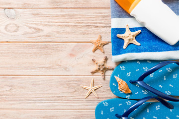 Top view of Beach flat lay accessories. sunscreen bottle with seashells, starfish, towel and flip-flop on wooden board background with copy space