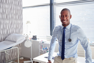 Portrait Of Smiling Male Doctor With Stethoscope Standing By Desk In Office