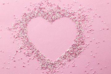 Pink and white pearly cake sprinkles shaped in a heart shape with empty space for text in the centre - Sprinkles on pink background