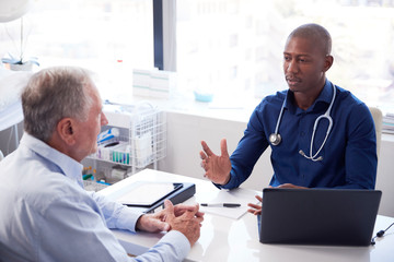 Senior Male Patient In Consultation With Doctor Sitting At Desk In Office