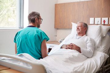 Obraz premium Surgeon With Digital Tablet Visiting Senior Male Patient In Hospital Bed In Geriatric Unit