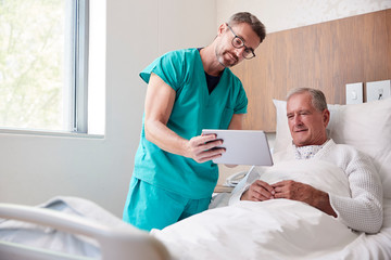 Obraz na płótnie Canvas Surgeon With Digital Tablet Visiting Senior Male Patient In Hospital Bed In Geriatric Unit