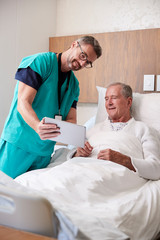 Obraz premium Surgeon With Digital Tablet Visiting Senior Male Patient In Hospital Bed In Geriatric Unit