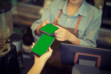 Customer using her smartphone and nfs technology to pay a barista for her purchase with phone at a cafe