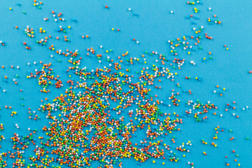 Fototapeta na wymiar Sprinkles on blue background - Little round cake topping sprinkles of many colours on bright blue - Top view
