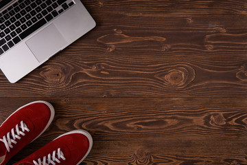 Top view of red suede sneakers and opened laptop standing on brown wooden planks