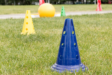 Bright plastic sports cones on the green grass outdoors to train the children's team. Sport coaching, training concept, gym time
