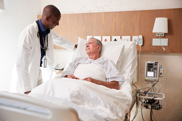 Doctor Visiting And Talking With Senior Male Patient In Hospital Bed 