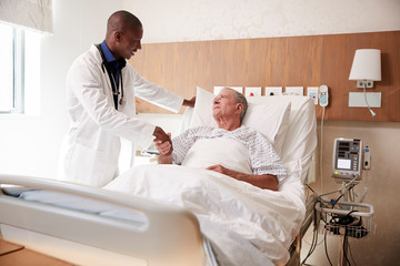 Obraz premium Doctor Shaking Hands With Senior Male Patient In Hospital Bed In Geriatric Unit
