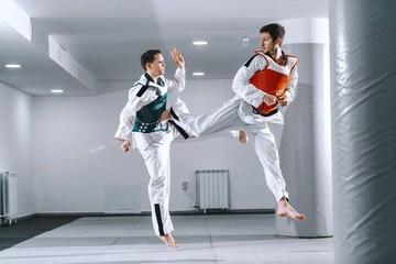 Two Caucasian sporty men sparring in tekwondo fittings barefoot.