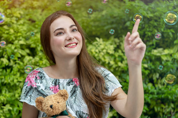 Beautiful caucasian woman hug teddy bear and playing soap bubbles outdoor at park. Relaxation and Freedom time.