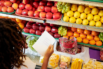 Woman with shopping list looking at shelves with fruits and berries at grocery store