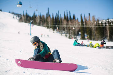 Young woman with a snowboard sitting on a snowy slope.