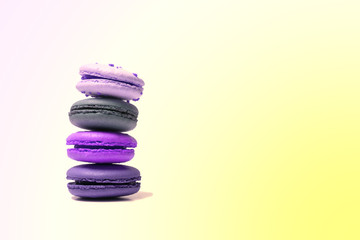 Fototapeta na wymiar Berry traditional french macaroons in violet colors are folded turret on top of each other. Gradient background with smooth transition from pastel yellow to gently lilac color. Copy space.