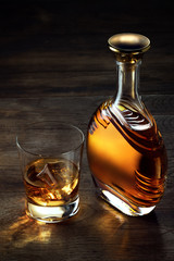 view of glass of  whiskey and a bottle aside on color wooden  background. 