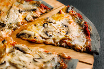 Pizza with champignons and chicken breast on black dough.