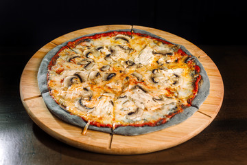 Pizza with champignons and chicken breast on black dough.