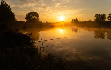 Fishing at foggy lake in the early morning just after golden sunrise