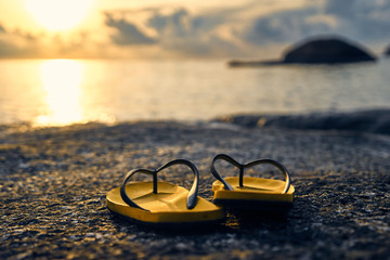 Fototapeta na wymiar Slippers on a rock by the sea on a background of dawn and sun 