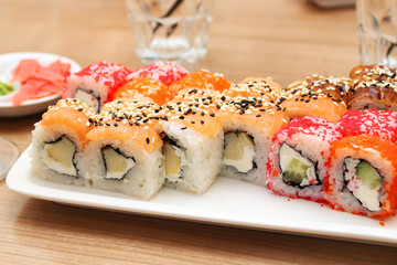 Sushi with fish, cheese and caviar on a white rectangular plate, empty glasses in the background