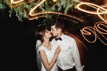 gorgeous elegant happy bride and stylish groom on the background glowing lights from garland in the evening