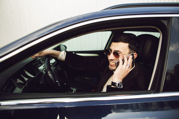Young bussinesman in suit and black glasses speaks by phone in his car. Bussines look. Test drive of the new car
