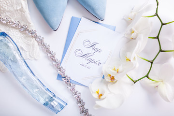 Wedding invitation surrounded with flowers, bride's shoes and jewellery. Morning of bride