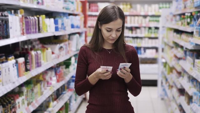 Young woman chooses between two products in supermarket, looks at camera, smiles