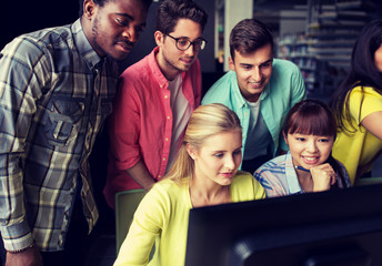 people, education, technology and school concept - group of happy smiling international students with computers at library in university