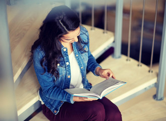 education, high school, university, learning and people concept - smiling student girl reading book sitting on stairs