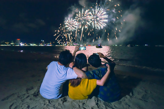 group of friends sitting and holding each others enjoy watching fireworks display on the beach