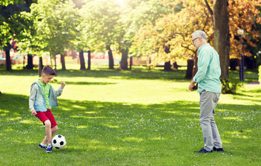 Obraz na płótnie Canvas family, generation, game, sport and people concept - happy grandfather and grandson playing football at summer park