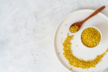 Bee pollen in a bowl and wooden spoon on white stone background
