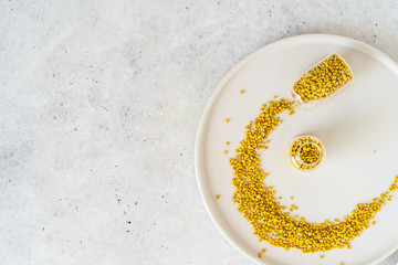 Bee pollen in glass vial on white stone background